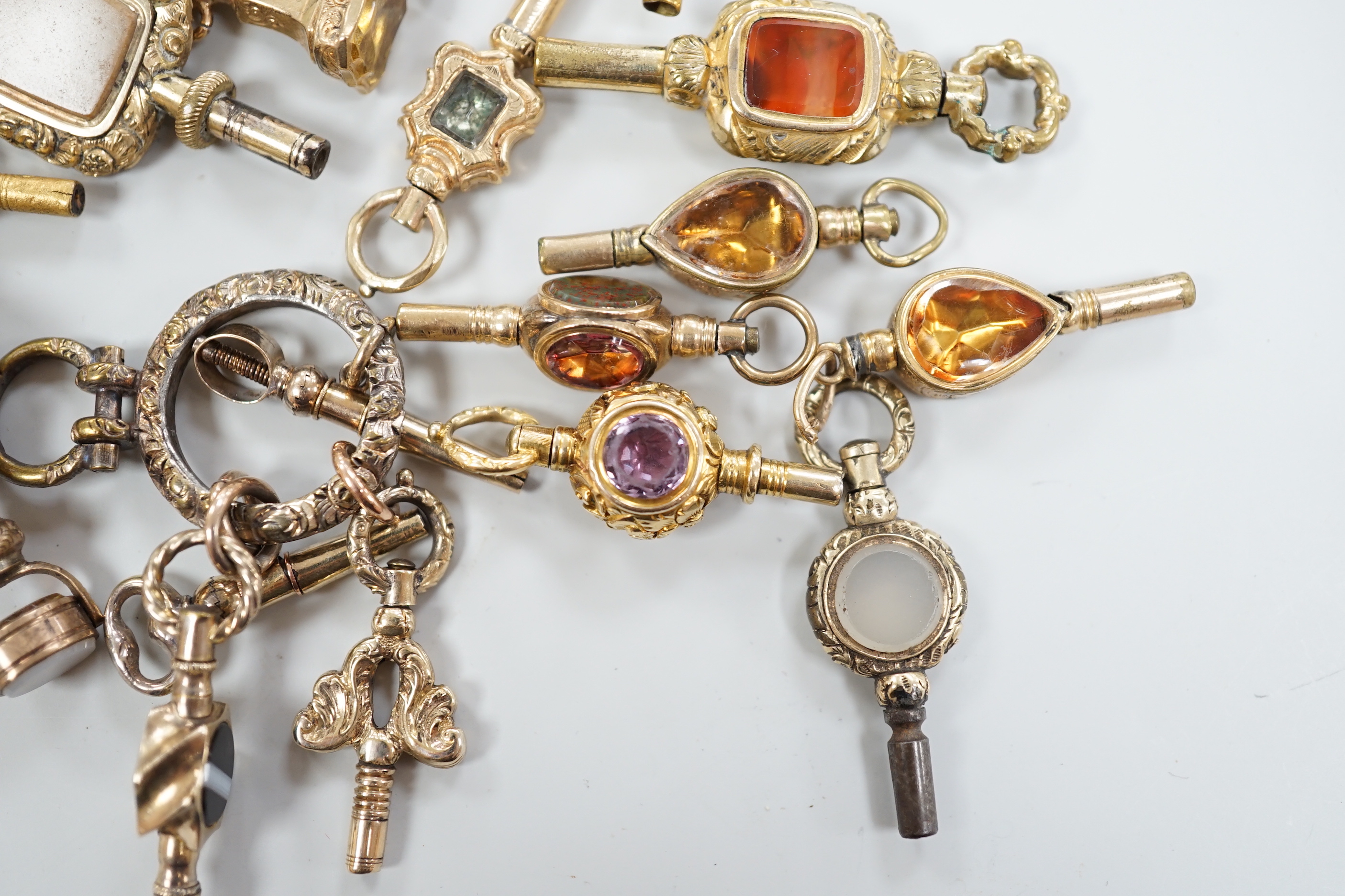 Sixteen assorted 19th century yellow metal overlaid and mainly gem set small watch keys, including chalcedony, citrine, amethyst, banded agate, bloodstone and a ring with four keys attached, largest 47mm.